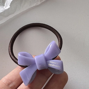 Close-up of a purple resin bow hair tie with silver France Handmade lettering detail