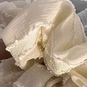 Detail of creamy white chiffon fabric with delicate frayed edges and pleated wave texture