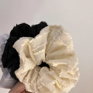 Detail of three large pleated hair scrunchies with frayed edges in beige, black, and grey