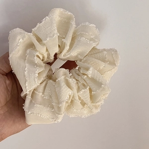 Close-up of cream oversized scrunchie featuring pleated fabric and soft raw edges