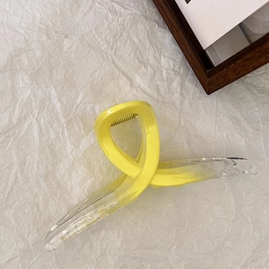 Macro di una grande pinza per capelli sfumata giallo limone su carta bianca elegante