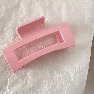 Macro shot of a glossy soft pink rectangular hollow hair claw clip on white textured paper