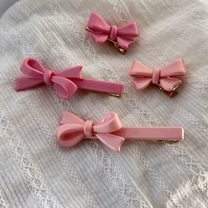 Vue détaillée de quatre barrettes nœuds roses sur dentelle blanche avec pinces dorées