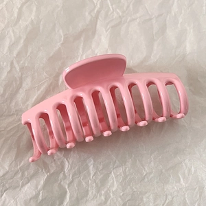 Close-up of a glossy pink shark hair claw clip on a textured white paper background