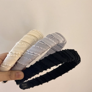 Close-up of pleated fabric headbands in white, grey, and black with handmade label