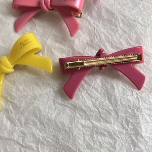 Détail de barrettes nœuds en rose et jaune vif avec clips métalliques dorés