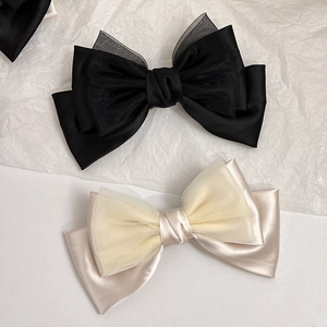Detailed close-up of large layered satin and organza bow hair clips in black and beige