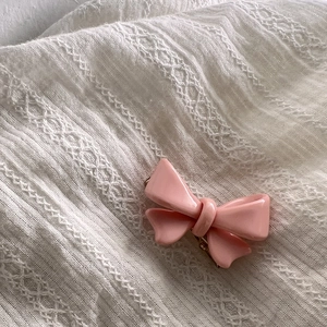 Barrette nœud rose avec finition brillante sur fond de dentelle blanche vue en détail
