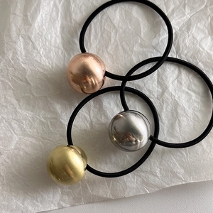 Gros plan sur trois élastiques à cheveux avec perles métalliques brossées or, argent et or rose