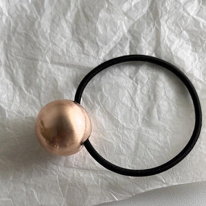Détail de la perle en métal brossé or rose sur un élastique à cheveux noir