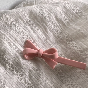 Gros plan détaillé d'une pince à cheveux rose brillant posée sur un tissu blanc texturé