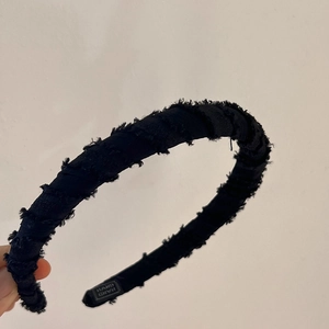 Detail of black fabric headband with fringe edges and Hand Made embroidery label