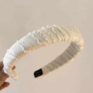 Detail of white fabric headband featuring raw frayed edges and elegant wrapped texture