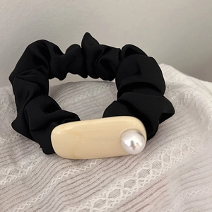 Close-up of black pleated hair scrunchie with resin detail and an elegant pearl inlay