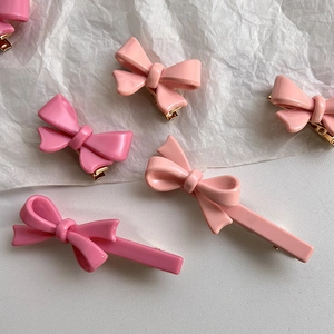 Vue détaillée de barrettes nœuds roses brillants avec clips dorés sur du papier blanc plissé