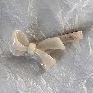 Dettaglio di un fermaglio a fiocco in acetato crema con finitura perlata e clip dorata