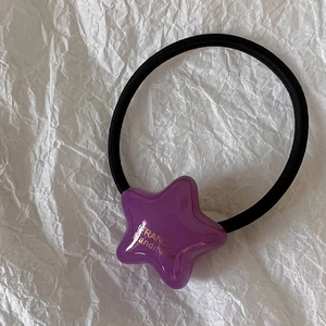 Détail d'un élastique à cheveux étoile en acrylique violet avec lettrage doré sur papier soie