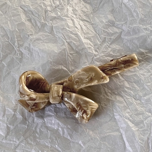 Dettaglio ravvicinato della molletta a fiocco in acetato beige con logo Handmade