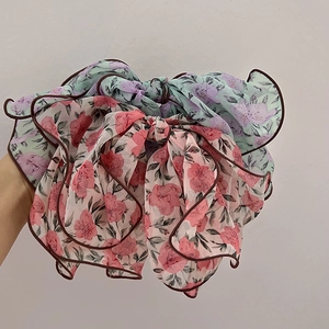 Close-up of two large floral chiffon bow hair clips in mint green and beige colors