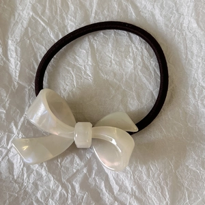 Detail of cream white acetate bow hair tie with pearlescent finish and black elastic band