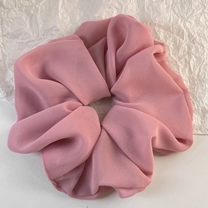 Detail eines rosa Chiffon-Haargummis mit eleganten Falten und feiner Textur im Detail