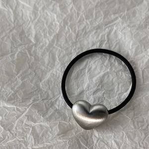 Detail of silver heart charm with brushed metal texture on a black elastic hair tie