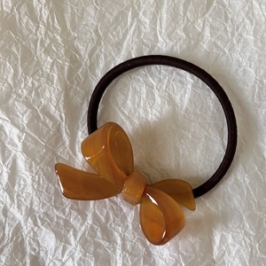 Detail of amber acetate bow hair tie with high-elasticity band on a white background