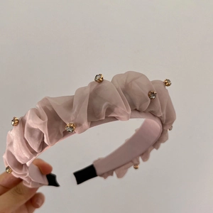 Dettaglio del cerchietto a pieghe rosa chiaro con strass scintillanti e tessuto di raso