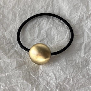Detailed macro view of the brushed gold metallic heart bead on a black elastic hair tie