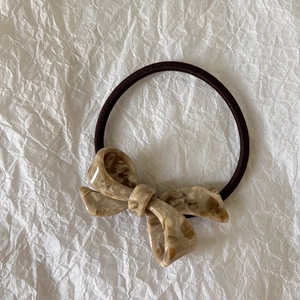 Detail of tortoiseshell bow hair tie with marble texture on white crinkled background