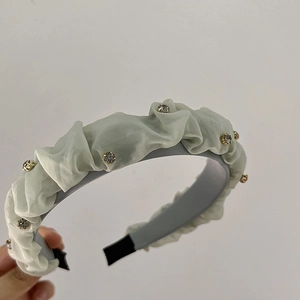 Dettaglio di un cerchietto in raso pieghettato grigio-verde con strass bianchi brillanti