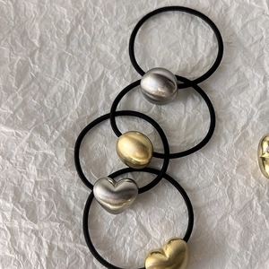 Detail of vintage heart-shaped and oval metal charms with brushed texture on black hair ties