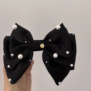 Gros plan sur la barrette nœud en satin noir avec perles blanches et badge doré