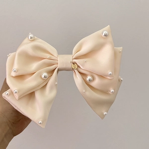 Détail de la pince à cheveux noeud en satin beige avec perles blanches et médaillon doré