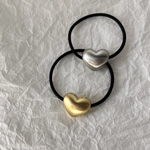 Detail of matte gold and brushed silver 3D heart charms on black elastic hair ties