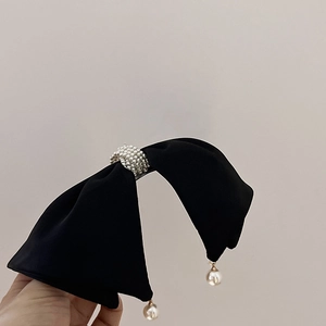 Detail of black satin bow hair clip with central pearls and elegant hanging pearl drops