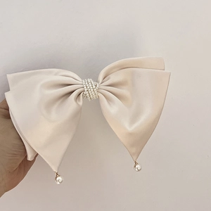 Detail of elegant cream satin bow hair clip with multi-layer pearls and hanging beads