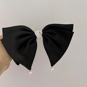 Close-up of elegant black satin bow hair clip with decorative pearls and pearl pendants