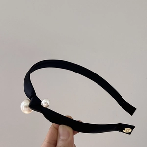 Detailed close-up of a black satin knotted headband featuring faux pearls and a handmade tag