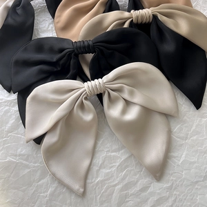 Detail showing oversized satin bow hair clips in black, khaki and beige colors