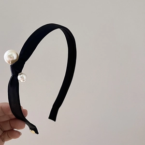 Detailed close-up of a black knotted headband featuring two elegant white pearls and a gold logo