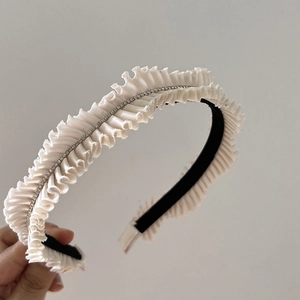 Detailed close-up of white pleated satin headband with sparkling rhinestones decoration