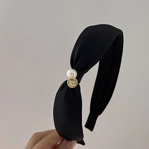 Detail of black knotted headband featuring a white pearl and gold 'Hand Made' charm