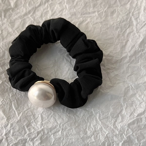 Détail d'un chouchou en tissu plissé noir avec une grande perle blanche et support doré