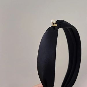 Detail of black satin knotted headband with white pearl and gold metal emblem