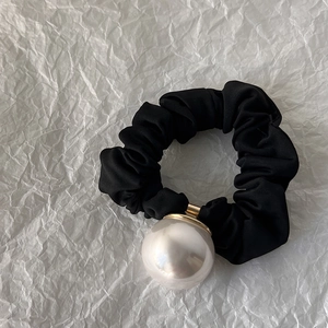 Détail d'un chouchou noir avec une perle blanche brillante sur papier crépon blanc