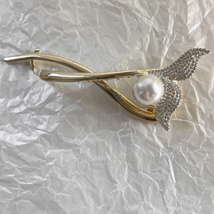 Détail d'une pince à cheveux dorée en forme de sirène avec strass scintillants et perle