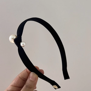 Detail view of black satin knot headband featuring elegant white pearls and gold metal accents