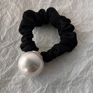 Détail d'un chouchou noir côtelé avec une grande perle blanche et un support doré