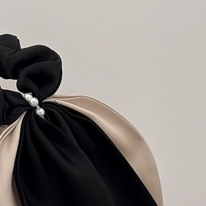 Close-up detail of satin scrunchie featuring black white contrast and pearl accents